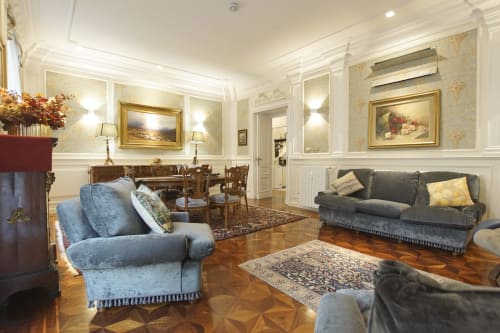 Elegante soggiorno della Suite Magna Mater a Roma con poltrona blu, divano grigio, camino, parquet e stile classico