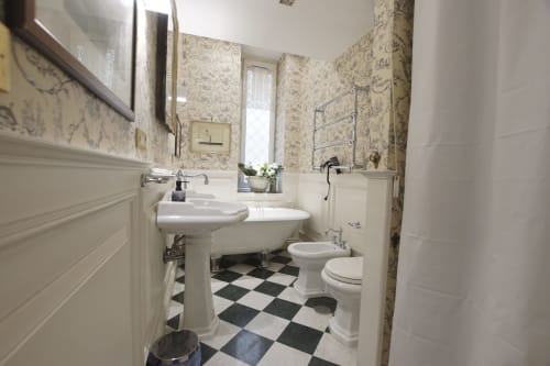 Bagno elegante nella Magna Mater Suite, Roma con lavabi a colonna, pavimento a scacchiera bianco e nero, e carta da parati toile