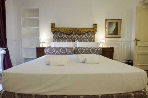 Camera da letto elegante nella Suite Magna Mater, Roma, con biancheria bianca, testata dorata ornamentale e arredamento classico