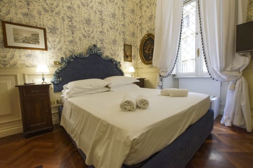 Camera da letto elegante nella Magna Mater Suite, Roma, con testata ornamentale, biancheria color crema, carta da parati damasco e stile classico