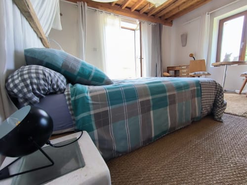 Chambre lumineuse avec literie carreaux turquoise, poutres en bois et accès terrasse à la Furanelle B&B à Saint-Étienne