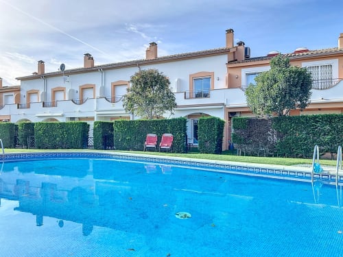Bright blue swimming pool at Estartit Rental in L'Estartit with white and peach townhouses, green hedges, and loungers