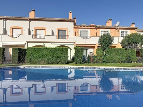 Estartit Rental cottages with blue swimming pool, green hedges, and Mediterranean architecture under clear sky
