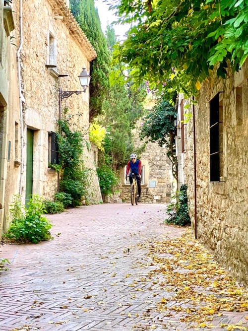 Charming cobblestone alley in L'Estartit with ivy-covered stone buildings and cyclist, showcasing rustic Mediterranean