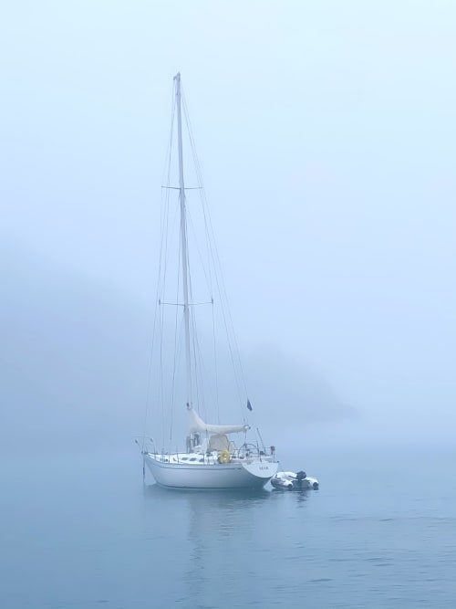 White sailboat anchored in calm fog-covered water near L'Estartit cottage rental with tender boat