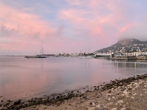 Serene coastal harbor view at L'Estartit with sailboats, rocky beach, and Mediterranean waterfront buildings at dusk