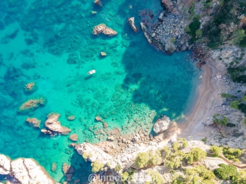 Aerial view of turquoise Mediterranean waters with rocky coastline, small boats, and sandy beach near L'Estartit, Spain