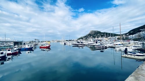 Serene marina in L'Estartit with moored sailboats, clear blue water, and coastal town nestled against hillside