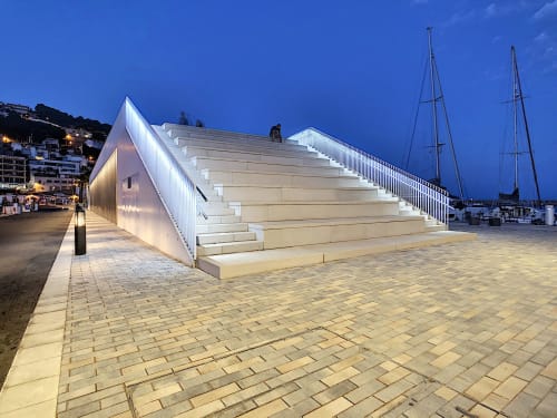 Modern illuminated waterfront staircase at L'Estartit marina with sailboats and coastal village backdrop at dusk