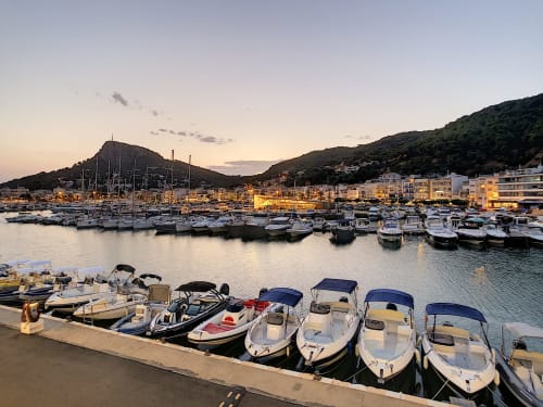 Estartit marina at sunset with white boats, blue-canopied rentals in foreground, hillside town and sailboats moored in harbor