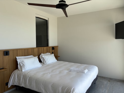 Chambre moderne à la Villa Aria Alto avec tête de lit en bois, literie blanche, ventilateur au plafond et porte noire à Pinarellu