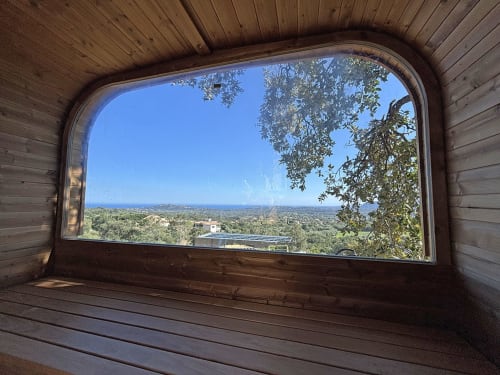 Vue panoramique sur la mer depuis la Villa Aria Alto aux Villas d'A Storia, Pinarellu, encadrée par une fenêtre en bois
