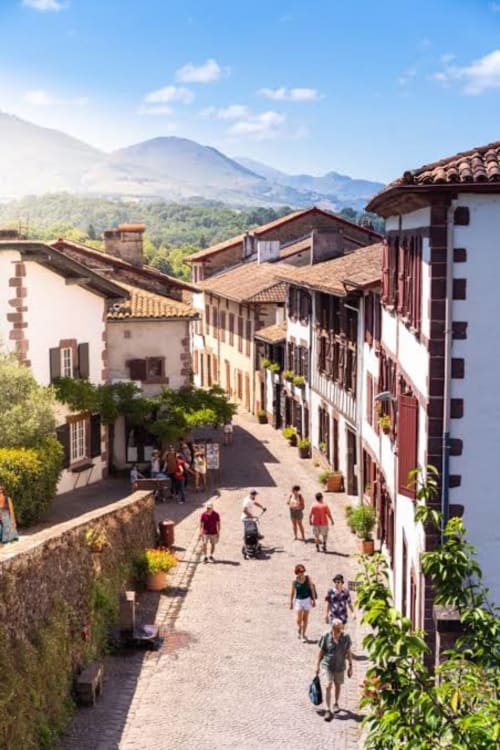 Colonial-style street in Gabillou with white buildings, mountains in background, guests strolling cobblestone plaza