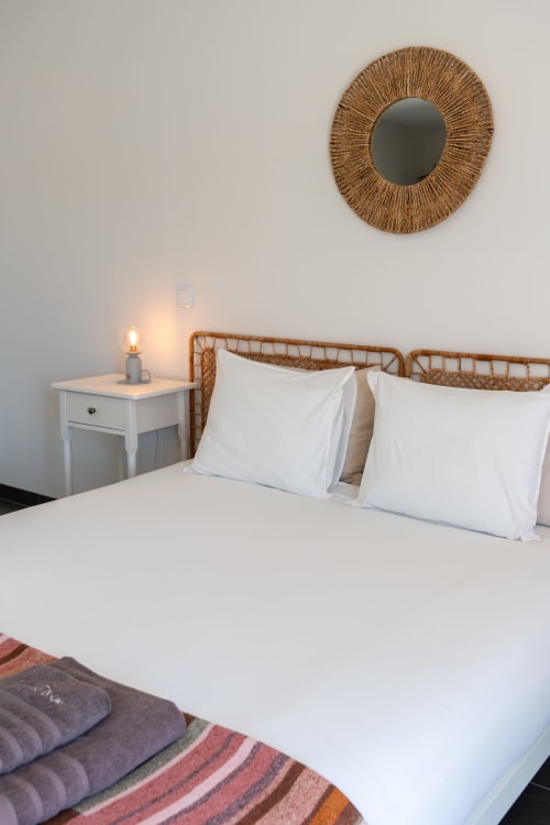 Bright bedroom at Canhoto Douro with rattan headboard, white pillows, wicker mirror, and bedside lamp in São Lourenço do