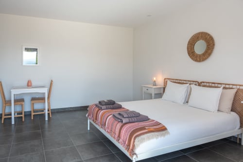 Bright bedroom at Canhoto Douro B&B in São Lourenço do Douro with queen bed, wicker mirror, white desk, and pool view window.