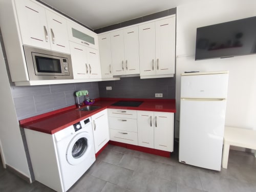 Cuisine moderne aux plans de travail rouges, armoires blanches et appareils en acier inoxydable à l'appartement VIVE Benalmádena