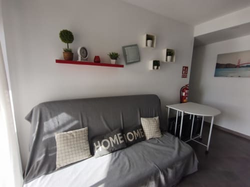 Chambre moderne à VIVE Benalmádena avec lit gris, étagère murale rouge, plantes en pot et vue sur la mer depuis la fenêtre