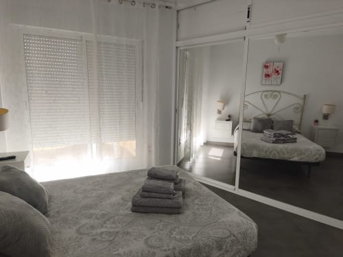 Chambre lumineuse à l'appartement VIVE Benalmádena avec armoire miroir, lit blanc et volets avec vue mer