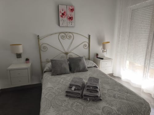 Chambre lumineuse de l'appartement VIVE Benalmádena avec tête de lit métallique, tables de nuit blanches et vue sur la mer depuis les portes-fenêtres du balcon.
