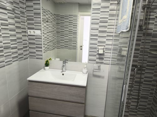 Salle de bain moderne aux murs carrelés de rayures gris et blanc, vasque blanche, miroir et douche à l'italienne à VIVE Benalmádena