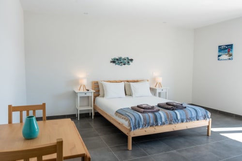 Bright bedroom at Canhoto Douro with wooden bed, white pillows, blue striped blanket, wooden dining table, and pool view in