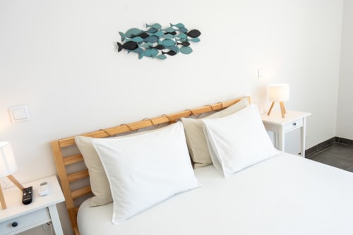 Bright bedroom at Canhoto Douro with wooden bed, white pillows, decorative fish wall art, and bedside table with lamp
