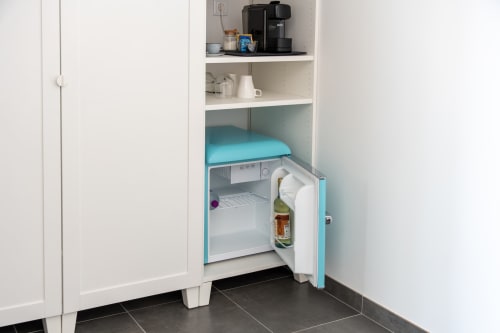 Compact turquoise mini fridge open in white built-in cabinet at Canhoto Douro guesthouse, with coffee maker and tea amenities