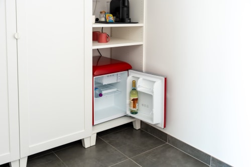 Red compact refrigerator with wine bottle in guest room at Canhoto Douro, São Lourenço do Douro