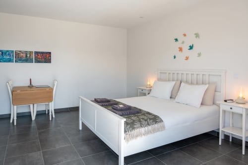 Bright bedroom at Canhoto Douro B&B with white bed, wooden desk, and decorative leaf wall art, pool view
