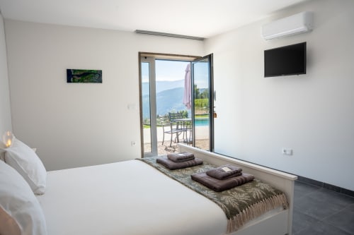 Modern bedroom at Canhoto Douro with white bed, mountain and pool views through glass doors, flat-screen TV, and terrace