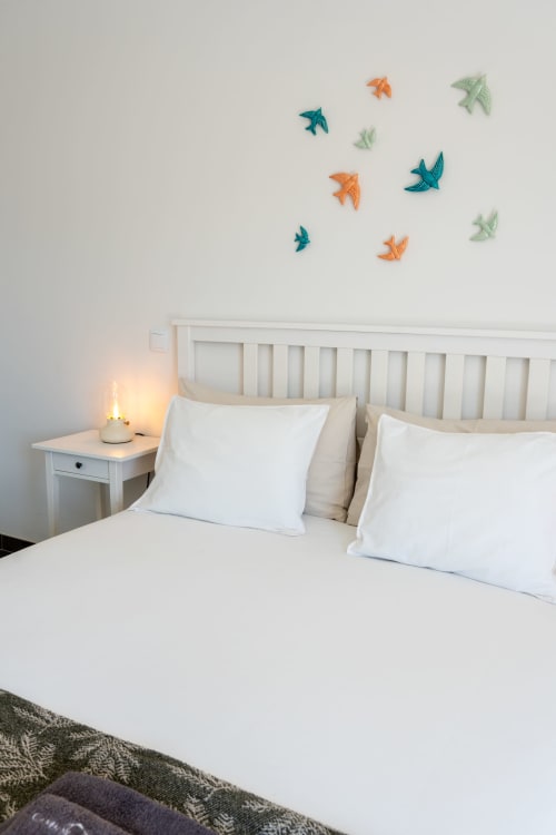 Bright bedroom at Canhoto Douro with white bedding, nightstand lamp, and colorful bird wall decorations