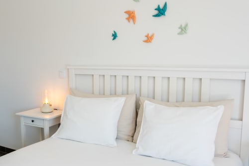 Bright bedroom at Canhoto Douro with white bedding, decorative paper birds on wall, and nightstand lamp in São Lourenço do