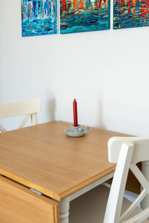 Wooden dining table with white chairs and red candle at Canhoto Douro B&B in São Lourenço do Douro, with colorful artwork