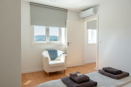 Bright bedroom at Canhoto Douro cottage with white armchair, mountain views, wooden floors, and rolled towels