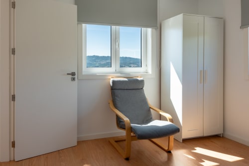Bright bedroom at Canhoto Douro cottage with wooden chair, wardrobe, mountain views through window, wooden flooring, and