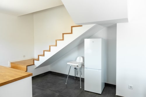Modern kitchen area under wooden stairs in Casa da Eira cottage at Canhoto Douro, with white refrigerator and black tiled
