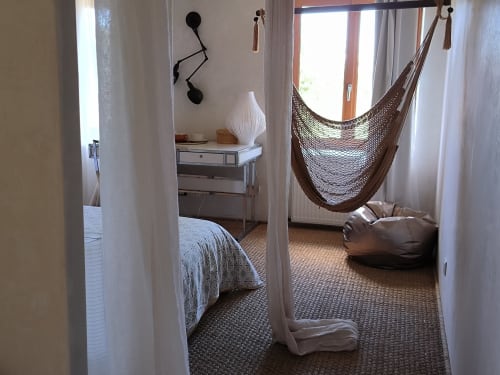 Chambre du gîte Furanelle à Saint-Étienne avec lit, chaise hamac, table de nuit et accès balcon vue montagne