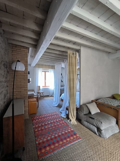 Chambre spacieuse de la Furanelle B&B Saint Étienne avec poutres apparentes, lit de repos, séparation textile et tapis motif rouge