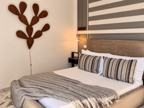 Modern bedroom at HABITARE Lecce with striped pillows, cactus wall art, and city view in Salento, Italy