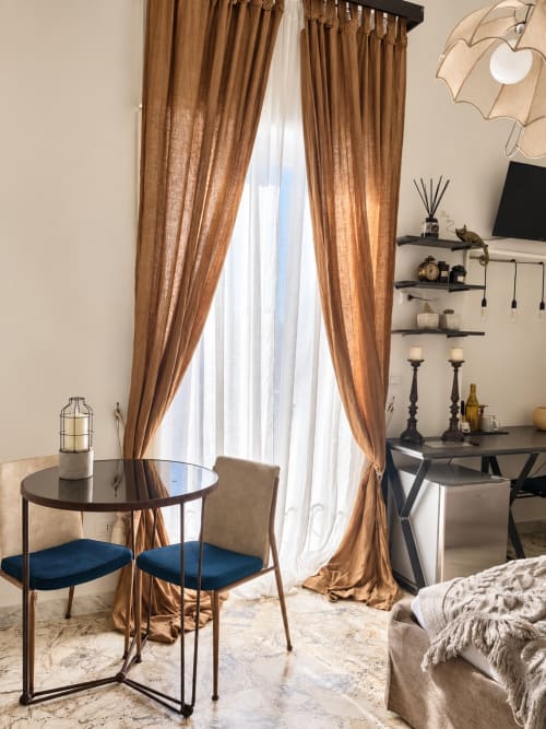 Elegant bedroom at HABITARE Lecce with golden curtains, round table with blue chairs, and city view from balcony
