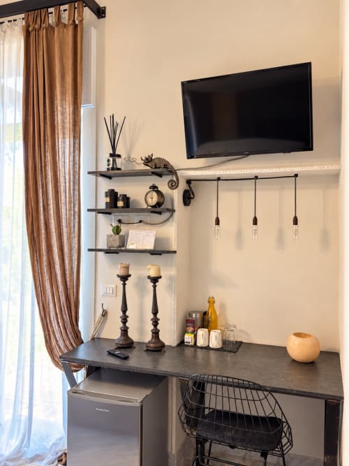 Modern hotel desk at HABITARE Lecce with wall-mounted TV, shelving, pendant lights, and work area overlooking Lecce city view