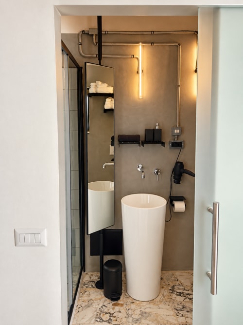 Modern bathroom in HABITARE Lecce hotel room with white cylindrical sink, taupe walls, and ambient lighting