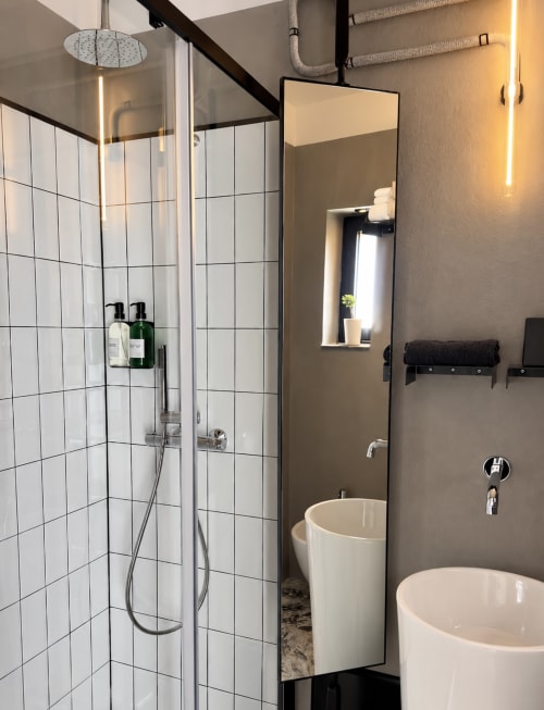 Modern bathroom in Lecce hotel with white tiled shower, pedestal sinks, and warm lighting accents