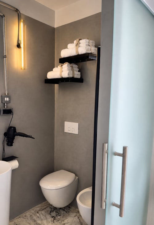 Modern bathroom at HABITARE Lecce with wall-mounted towel shelves, wall sconce lighting, white toilet, and marble flooring