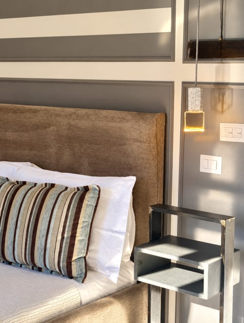 Modern bedroom at HABITARE Lecce with brown upholstered headboard, striped pillow, pendant lamp, and wooden step stool in