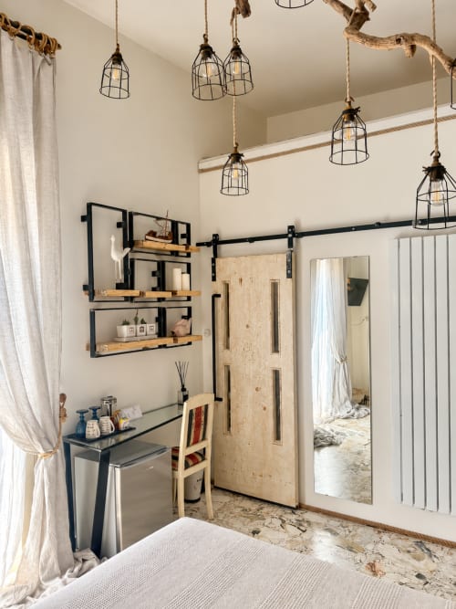 Camera eco-moderna ad HABITARE Lecce con lampade a sospensione industriali, porta a soffietto nera, ripiani in legno e stile contemporaneo