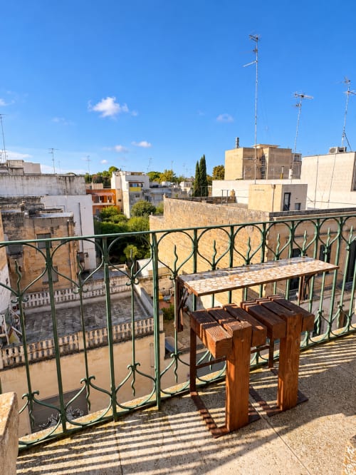 Terrazza con elegante ringhiera verde che domina i tetti e gli edifici storici di Lecce sotto un cielo azzurro limpido