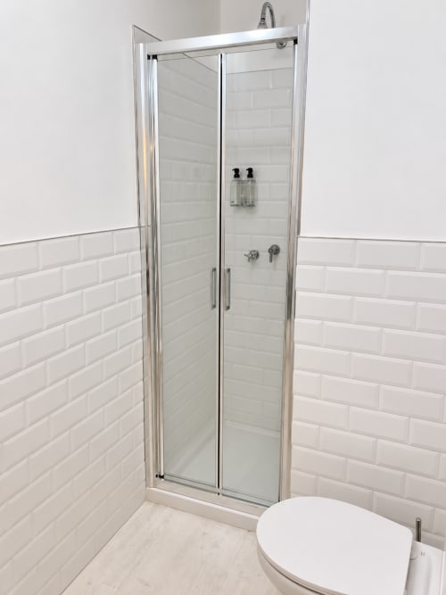 Bagno moderno con piastrelle bianche, box doccia in vetro temperato e rubinetteria cromata dell'hotel HABITARE Lecce