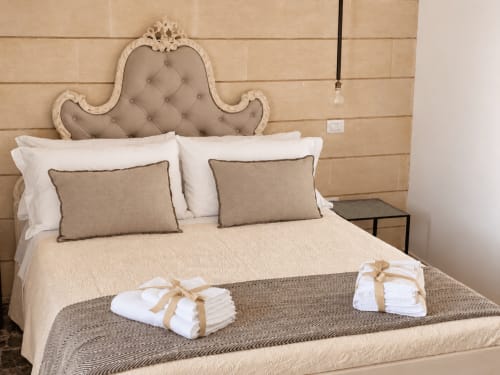 Camera da letto elegante presso HABITARE Lecce con testata ornamentale, cuscini bianchi, dettagli beige e set di asciugamani benvenuto