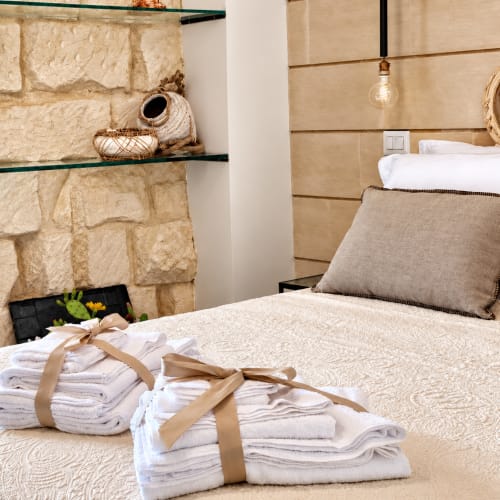 Petra Superior Room ad HABITARE Lecce con muri in pietra, letto, asciugamani impilati e arredamento rustico